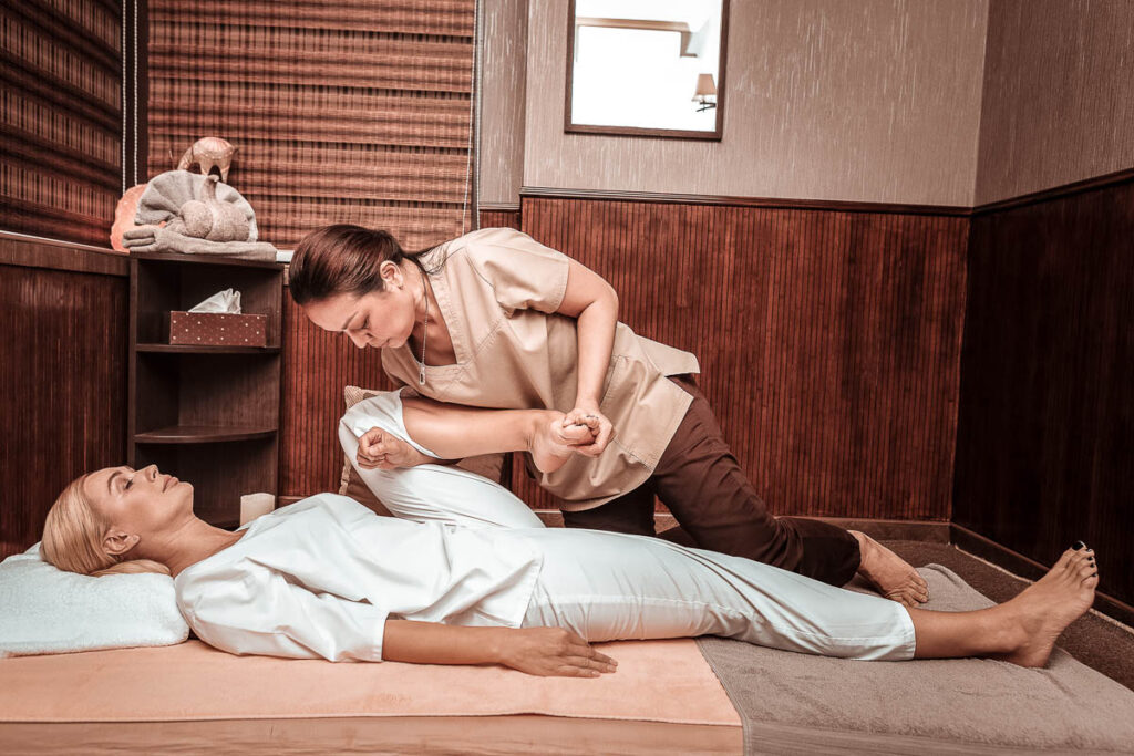 Stretching legs. Strong masseuse holding her clients foot and putting hand under her knee doing her thai massage, one of the cheapest massage prices in thailand