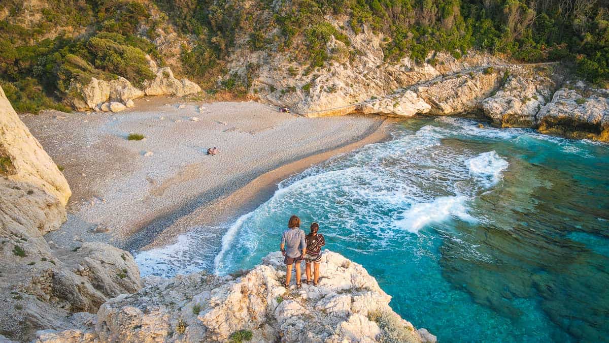 couple standing on rock in front of a beautiful beach in Greece