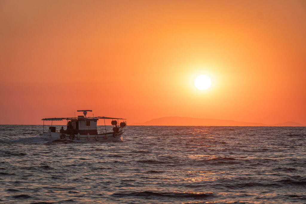 boat passing in front of the setting sun by a greek island